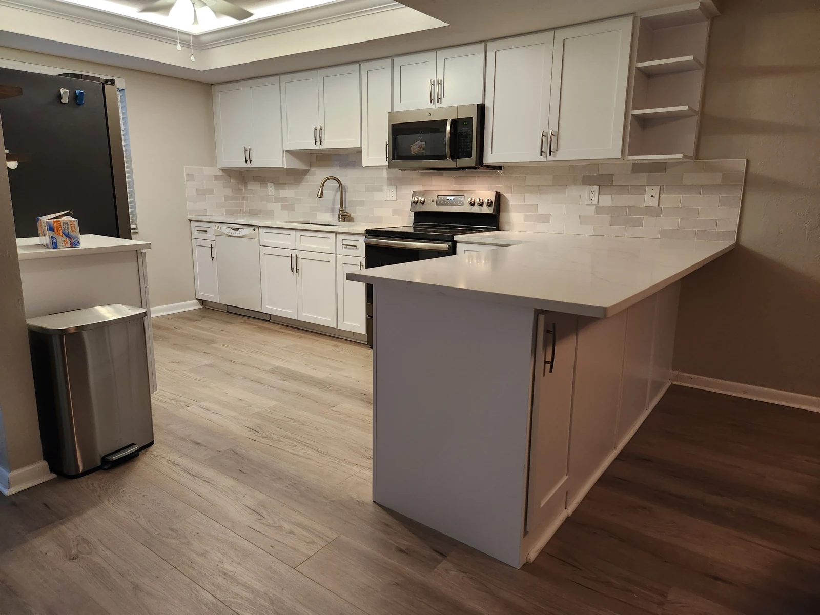 White kitchen with updated cabinet fronts, dark pulls, open shelving and a gray peninsula