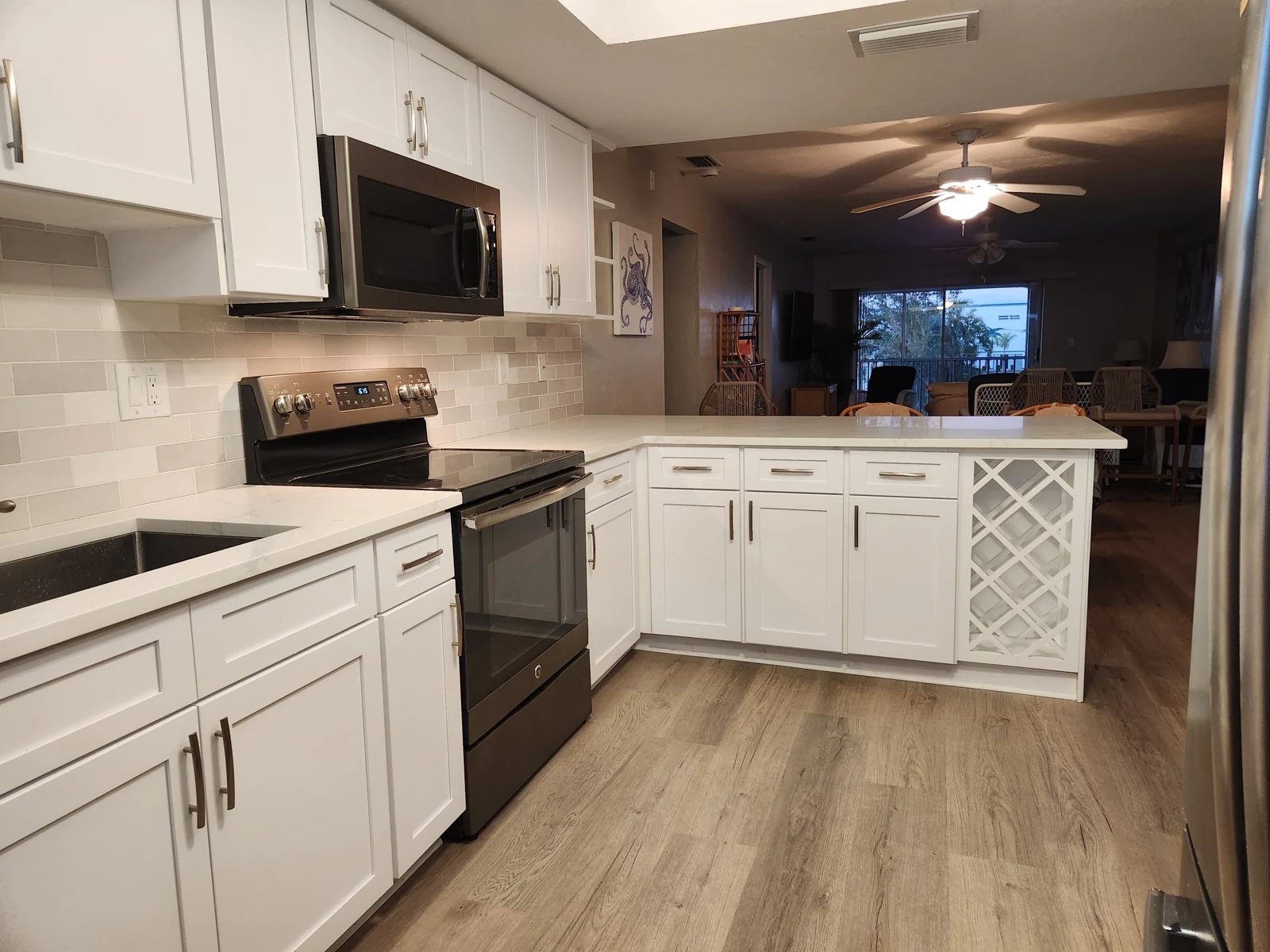 Refaced white shaker kitchen cabinets seen from the side, with quartz counters, a tiled backsplash and an open peninsula