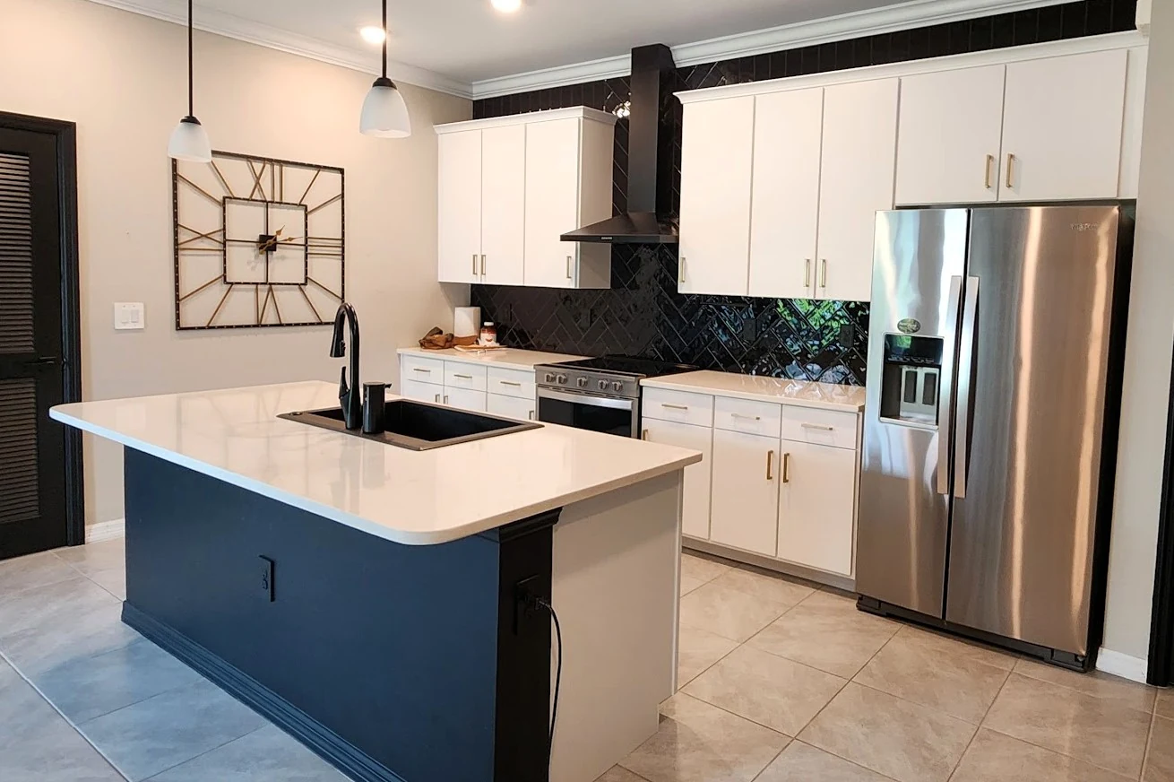 The same kitchen after the update, with flat white door fronts, gold pulls and a navy island base